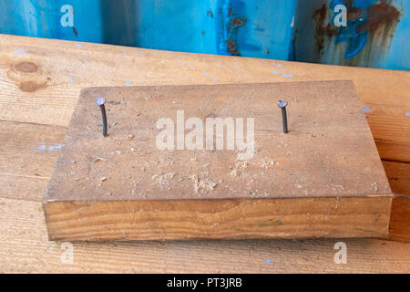 Holzblock mit zwei Nägel in Workshop cabinetry Reparatur Werkbank mit blauen Wand Stockfoto