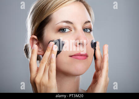 Porträt eines lächelnden jungen Frau Anwendung Aktivkohle Maske auf dem Gesicht Stockfoto
