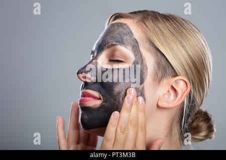 Close-up eine glückliche Frau mit Aktivkohle Maske auf grauem Hintergrund Stockfoto