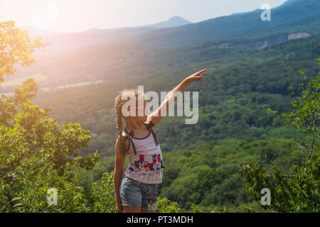 Das Mädchen sitzt auf dem Berg und in die Ferne schaut. Stockfoto