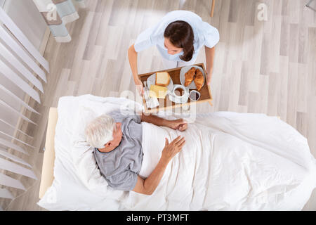 Ansicht der weiblichen Krankenschwester mit Speisen zu den älteren männlichen Patienten in der Klinik Stockfoto