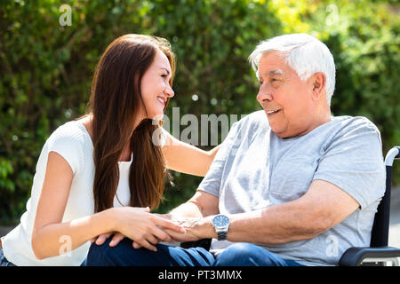 Glückliche junge Frau auf der Suche nach Ihrem Vater Sitzen auf Rollstuhl an im Freien Stockfoto