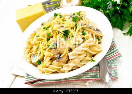 Fusilli mit Champignons in Rahmsauce, Petersilie und geriebenem Käse in einer Schüssel auf dem Handtuch gegen Licht Holzbrett Stockfoto