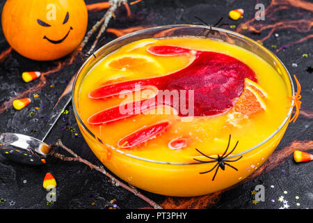 Ghoul orange Punch mit blutigen Eis Hand in eine Glasschüssel auf dunklen halloween Hintergrund Stockfoto