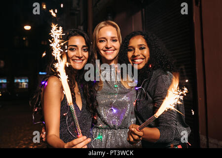 Drei junge weibliche Freunde genießen Sie Silvester mit Feuerwerk in der Nacht Stockfoto