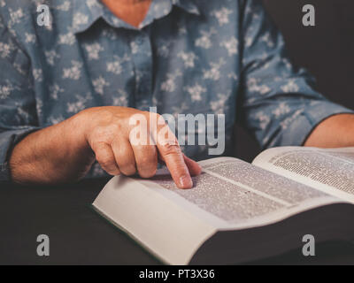 Alte Frau lesen dickes Buch zu Hause. Großmutter mit Bibel. Konzentriert Altersrentner mit Falten der Hände aufmerksam folgt Finger auf Pape Stockfoto