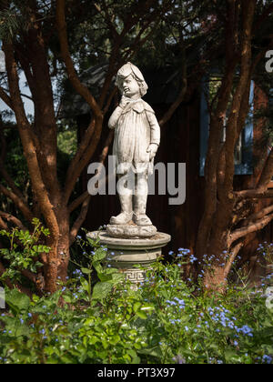 Statue eines Jungen aus Stein in einem Garten an einem sonnigen Tag im Sommer Stockfoto