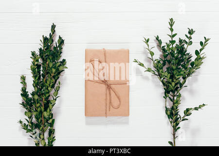 Vorhanden, in Handwerk Papier gewickelt und gebunden, mit Schnur liegt auf weiße Holztisch neben Niederlassungen der grünen Buchsbaum, Ansicht von oben. Im skandinavischen Stil Chris Stockfoto