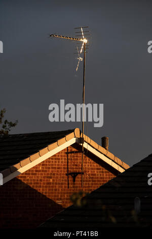 Ungewöhnliche Sonnenlicht in der Dämmerung leuchtet auf Dächer auf einer Wohnsiedlung Drehen der Himmel dunkel und Malerei die Gebäude mit einem orangefarbenen Leuchten, Großbritannien Stockfoto