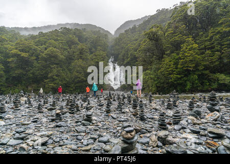 Touristen zu Fuß durch rock Cairns an Fantail fällt auf einen regnerischen Tag, Mount Aspiring National Park, West Coast Region, South Island, Neuseeland, Stockfoto