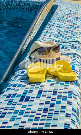 Stroh Hut, Sonnenbrille und Gelb flip-flops am Pool in den Badeort, senkrecht. Stockfoto