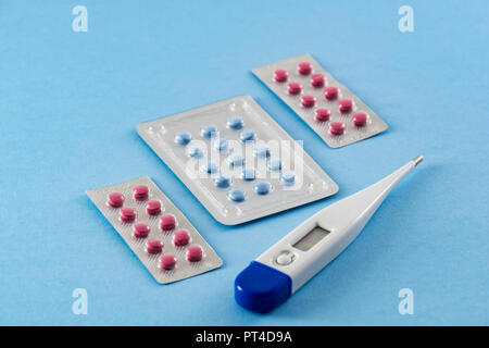 Blister blau und rosa Pillen und Elektronische Digitalthermometer auf blauem Hintergrund - Gesundheitswesen und medizinische Konzept Stockfoto