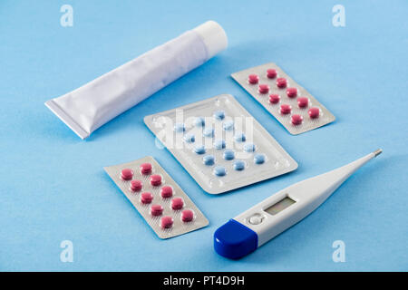 Blister blau und rosa Pillen, weiße Salbe tube und Elektronische Digitalthermometer auf blauem Hintergrund - Gesundheitswesen und medizinische Konzept Stockfoto