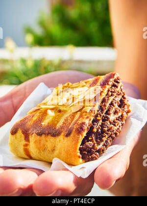 Eine weibliche Hand, die einen Teil der Kokosh, Schokolade roll Gebäck, von der traditionellen jüdischen Gebäck. Stockfoto