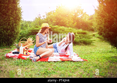 Zwei schöne junge Mädchen sitzen auf einer Sommer Picknick im Park bei Sonnenuntergang und Äpfel Stockfoto