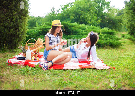 Zwei schöne junge Mädchen sitzen auf einer Sommer Picknick im Park bei Sonnenuntergang und Äpfel Stockfoto