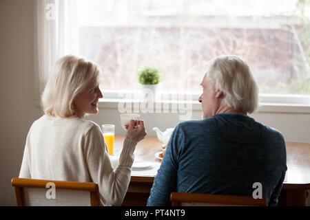Rückansicht des Happy senior altes Ehepaar sitzt am Esstisch Tee trinken und reden zu Hause, lächelnd im mittleren Alter reifen Familie genießen Kaffee und p Stockfoto