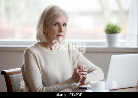 Nachdenklich ernsten reife ältere Frau denken der Problem Lösung in der Nähe von Laptop, fokussierte alte Dame mittleren Alters oder beten Gefühl anx besorgt Stockfoto