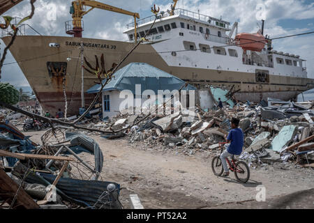 Palu, Sulawesi, Indonesien. 15 Okt, 2018. Eine lokale gesehen auf einem Fahrrad neben einem gestrandeten Schiff. Eine tödliche Erdbeben der Magnitude 7,5 und der Tsunami Welle verursacht durch die Stadt von Palu und viel von der Gegend in Zentral-sulawesi zerstört hat. Nach Ansicht der Beamten, die Zahl der Todesopfer von verheerenden Erdbeben und Tsunami steigt auf 1.480, rund 800 Menschen in Krankenhäuser sind schwer verletzt und rund 62.000 Menschen in 24 Flüchtlingslagern rund um die Region vertrieben worden. Credit: Hariandi Hafid/SOPA Images/ZUMA Draht/Alamy leben Nachrichten Stockfoto