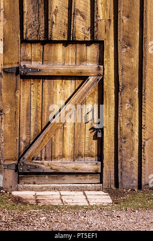 Eine schwere Holztür in einem alten Gebäude - Haus, Scheune, etc. Die Tür ist von außen mit einem silbernen metall Vorhängeschloss auf ein Metall Schraube gesperrt. Die b Stockfoto