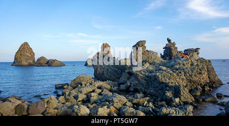 Leute auf einem Basaltfelsen am Cyclops Inseln, Aci Trezza, Gemeinde Aci Castello, Catania, Sizilien, Italien Stockfoto