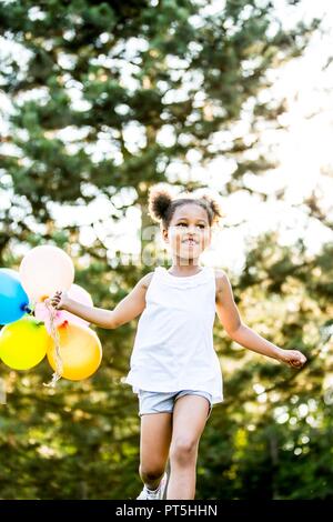 Mädchen in Bündeln mit Luftballons im Park, ein Lächeln auf den Lippen. Stockfoto