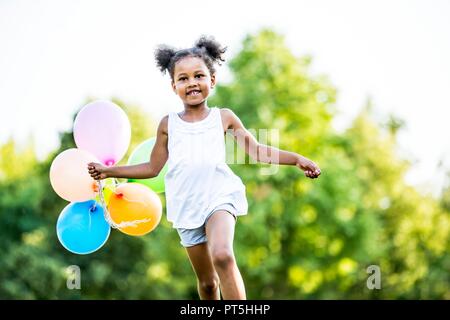 Mädchen in Bündeln mit Luftballons im Park, ein Lächeln auf den Lippen. Stockfoto