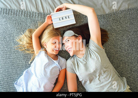 Halten Sie sie fest. Süße liebevolle emotionale Frau ihre Tochter fest umarmt, während die Ausgaben der Morgen im Bett und das Gefühl glücklich. Nase an Nase. Holding lig Stockfoto