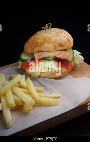 Große Fische Burger mit Forellenfilet und Salat auf einem Brett mit Pommes frites serviert. Stockfoto