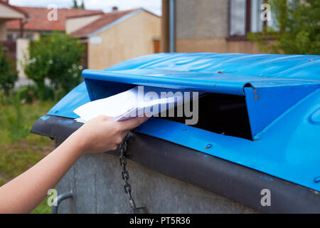 Junge Frau werfen Papierdokumente in einem blauen Container für sortierten Abfall Stockfoto