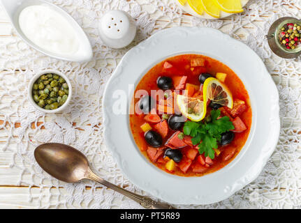 Traditionelle russische Suppe Solyanka mit Fleisch, Wurst, Gemüse, Kapern, Essiggurken und Oliven mit Zitrone, Gewürzen und Gewürzen. Mit saurer Crea serviert. Stockfoto