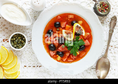 Traditionelle russische Suppe Solyanka mit Fleisch, Wurst, Gemüse, Kapern, Essiggurken und Oliven mit Zitrone, Gewürzen und Gewürzen. Mit saurer Crea serviert. Stockfoto