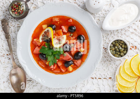 Traditionelle russische Suppe Solyanka mit Fleisch, Wurst, Gemüse, Kapern, Essiggurken und Oliven mit Zitrone, Gewürzen und Gewürzen. Mit saurer Crea serviert. Stockfoto