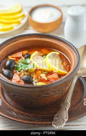 Traditionelle russische Suppe Solyanka mit Fleisch, Wurst, Gemüse, Kapern, Essiggurken und Oliven mit Zitrone, Gewürzen und Gewürzen. Mit saurer Crea serviert. Stockfoto