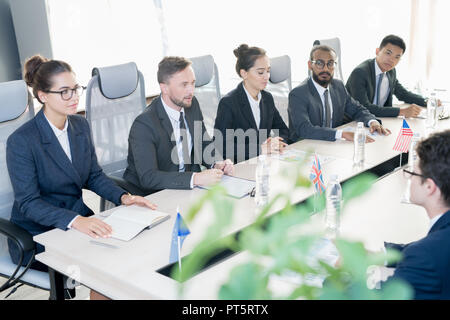 Gruppe zuversichtlich, den Vertretern der einzelnen Länder in formalen sitzen in Reihe am Konferenztisch mit nationalen Flaggen und Dokumente und führenden Verhandlungen Stockfoto
