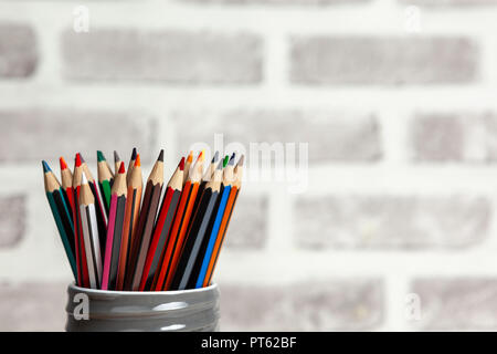 Satz von Buntstifte in einem grauen Schraube oben Tongefäß, gegen eine blured brick wall gespeichert Stockfoto