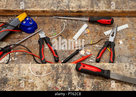 Spitzzange und verschiedene elektrische Handwerkzeuge auf einer alten hölzernen Werkbank mit Schrotten des Kupfer Kabel und Anschlüsse Stockfoto