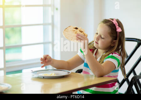 Kind essen Pfannkuchen im sonnigen Küche. Frühstück für Kinder. Kleines Mädchen mit Pfannkuchen mit frischer Schlagsahne in den frühen Morgenstunden. Stockfoto