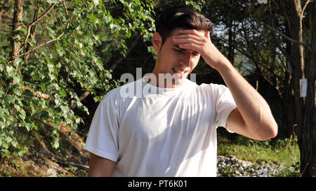 Junge Mann in der Natur leiden unter Kopfschmerzen. Stockfoto