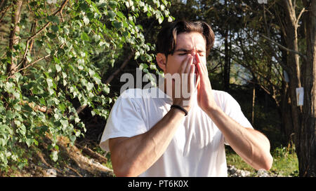 Junger Mann Niesen in der Natur im weißen T-Shirt Stockfoto