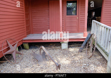 Zurück von alten, roten Holzhaus. Two-Bit Taylor Inn mit Eisen Texas Stern, & alte Wagenrad. Tür öffnen. Chestnut Square Historic Village, McKinney Texas. Stockfoto