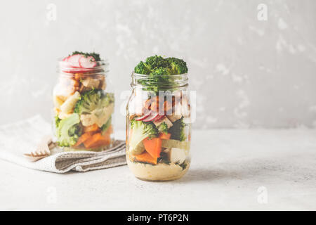 Gesunde hausgemachte Mason Jar-Salat mit gebackenem Gemüse, Hummus, Tofu und Kichererbsen. Gesunde Ernährung, Entgiftung, sauber Essen oder vegane Konzept. Stockfoto