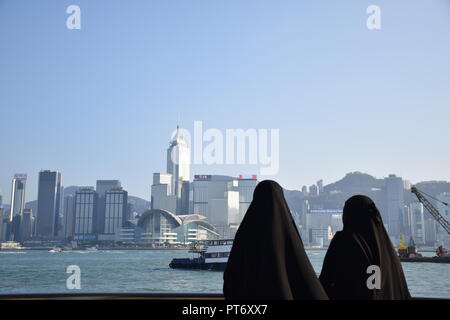 Mädchen gekleidet mit Burka vor der Skyline von Hong Kong Island vom Tsim Sha Tsui Promenade in Hongkong, China Stockfoto