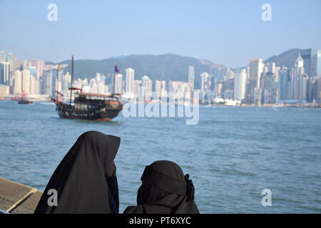 Mädchen gekleidet mit Burka vor der Skyline von Hong Kong Island vom Tsim Sha Tsui Promenade in Hongkong, China Stockfoto