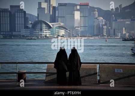 Mädchen gekleidet mit Burka vor der Skyline von Hong Kong Island vom Tsim Sha Tsui Promenade in Hongkong, China Stockfoto