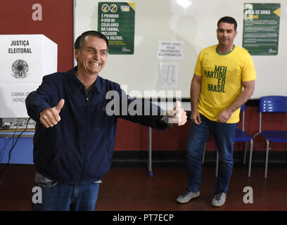 Rio de Janeiro, Brasilien. 07 Okt, 2018. 07 Oktober 2018, Brasilien, Sao Paulo: Jair Bolsonaro (L), ultra-rechten Kandidaten für den Posten des brasilianischen Präsidenten, lacht nach seiner Stimmabgabe im Wahllokal in der Stadt Schule Rosa da Fonseca, in Vila Militar, westlich von der Stadt. Im Hintergrund ist sein Sohn Flavio Bolsonaro. Mitten in einer schweren Krise, die Präsidentenwahl hat in Brasilien begonnen. Quelle: Fabio Teixeira/dpa/Alamy leben Nachrichten Stockfoto