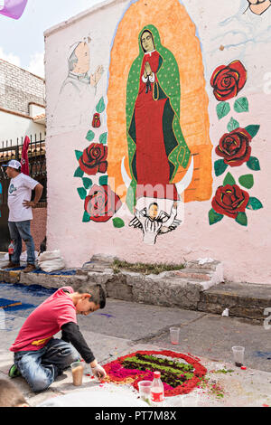 Ein Junge erstellt einen geblümten Teppich aus farbigem Sägemehl hergestellt und mit Blumen neben einem Wandgemälde von der Jungfrau von Guadalupe während der 8. Nacht Feier gestaltet markiert das Ende des Festes des Hl. Michael in der mexikanischen Stadt Uriangato, Guanajuato. Jedes Jahr schmückt die Stadt 5 km Fahrt mit religiösen Symbolen in der Vorbereitung für die Statue der Schutzheiligen durch die Stadt zu vorgeführt werden. Uriangato wurde eine internationale Sensation nach wowing Brüssel mit Ihren geblümten Teppich auf dem Brüsseler Grand-Place während der Belgien geblümten Teppich Festival angezeigt. Stockfoto