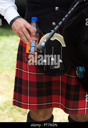 Scottish Bagpiper macht Pause und hält eine Flasche Irn Bru Stockfoto