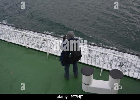 Amateur Fotograf mit der Kamera in der Hand auf Deck der Fähre zur Insel zwischen Oban und Castlebay Schottland mit ruhigen Meer Schaum im Hintergrund Stockfoto