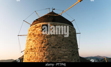Eine alte Steinmühle auf einem Berg, vor dem Hintergrund einer Bergkette und das Tal mit einem kleinen Städtchen mit weissen Häusern auf einer griechischen Insel Stockfoto